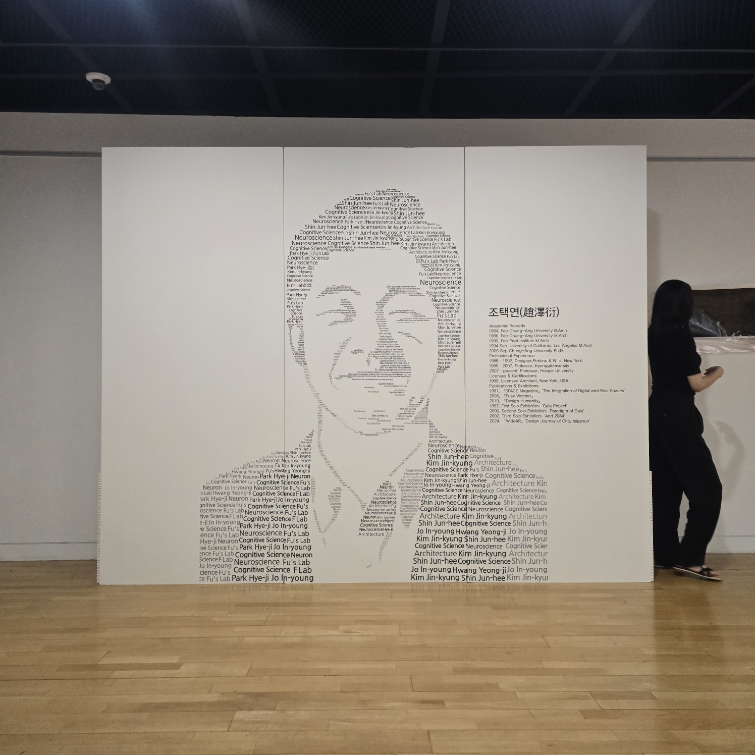화이트 표면에 인물 초상과 텍스트가 타이포그래피 기법으로 인쇄된 대형 3연 가벽. 우측에 '조택연(趙澤衍)' 제목과 이력 정보가 별도 패널로 부착되어 있으며, 전시 공간에 자립형으로 설치됨.