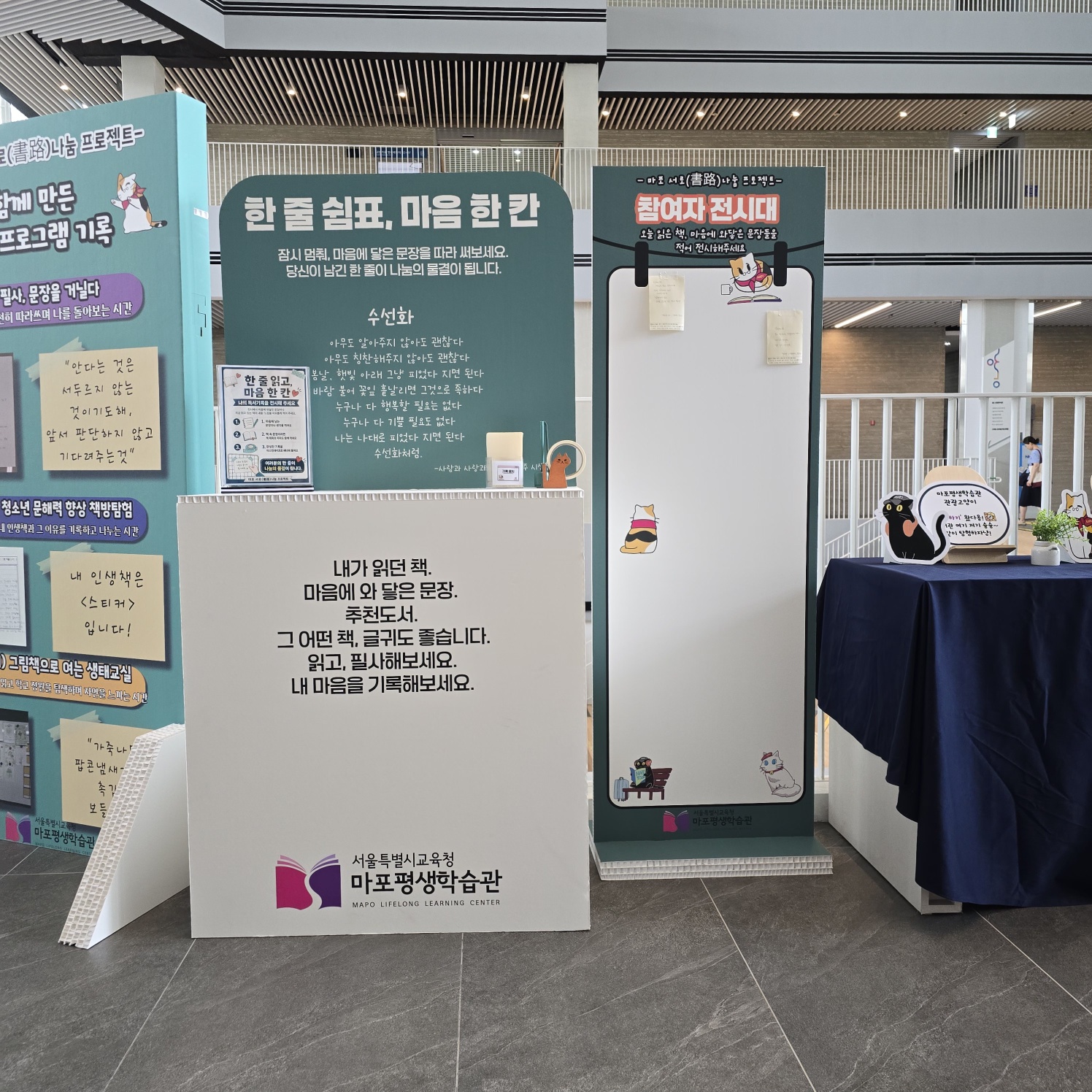 허니콤보드 병풍형 가벽 여러 면이 펼쳐진 모습. 좌측은 연한 청록색, 중앙은 짙은 청록색, 우측은 회백색 배경으로 각각 다른 내용의 안내문·일러스트가 컬러 인쇄됨. 수선화 시 안내, 독서 진시대 등 프로젝트 홍보 문구.