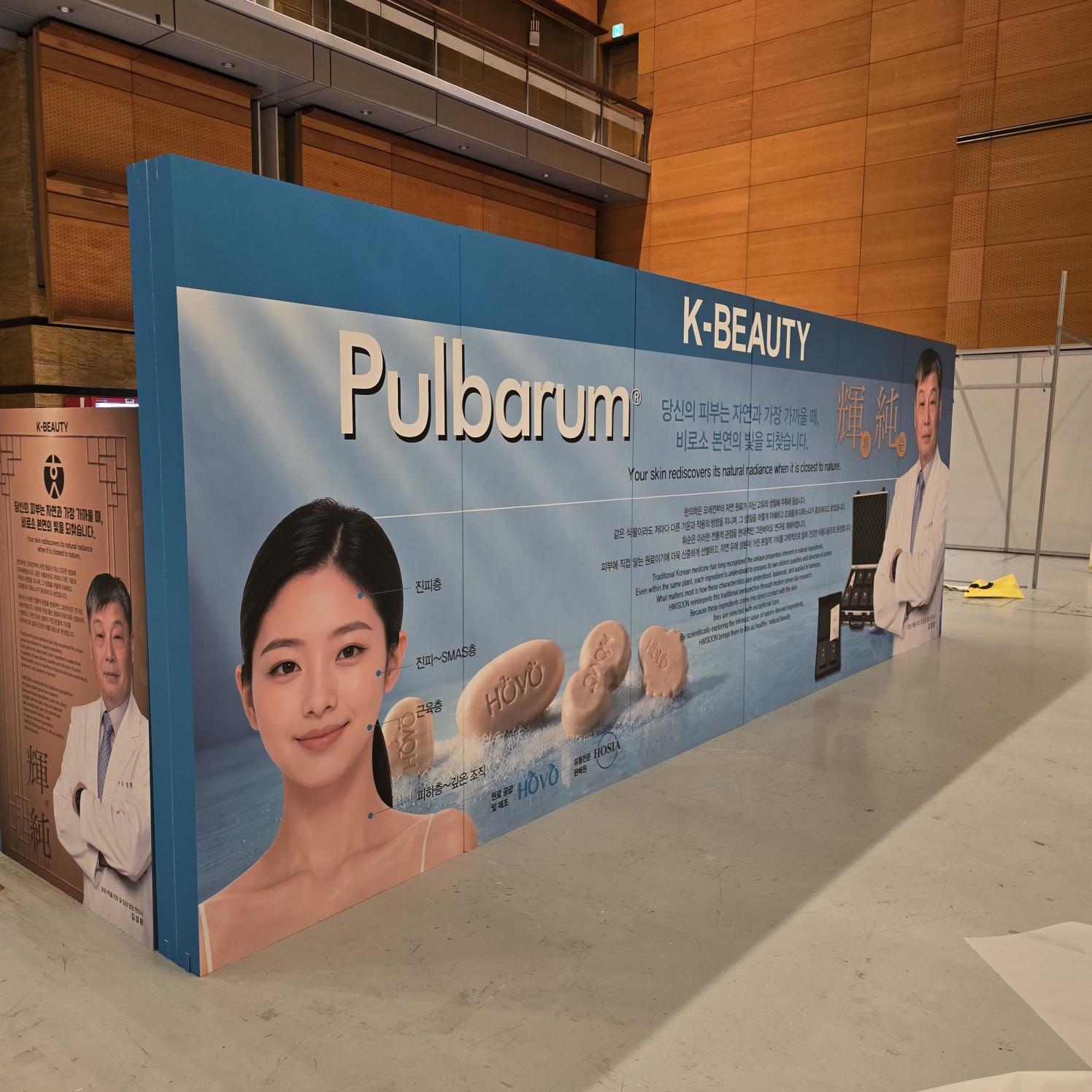 동일 배너 반대편. 청색 띠, 'K-BEAUTY', 'Pulbarum' 로고, 여성 모델 얼굴과 제품 이미지, 한글·영문 설명문, 하단 자연 풍경 사진 인쇄