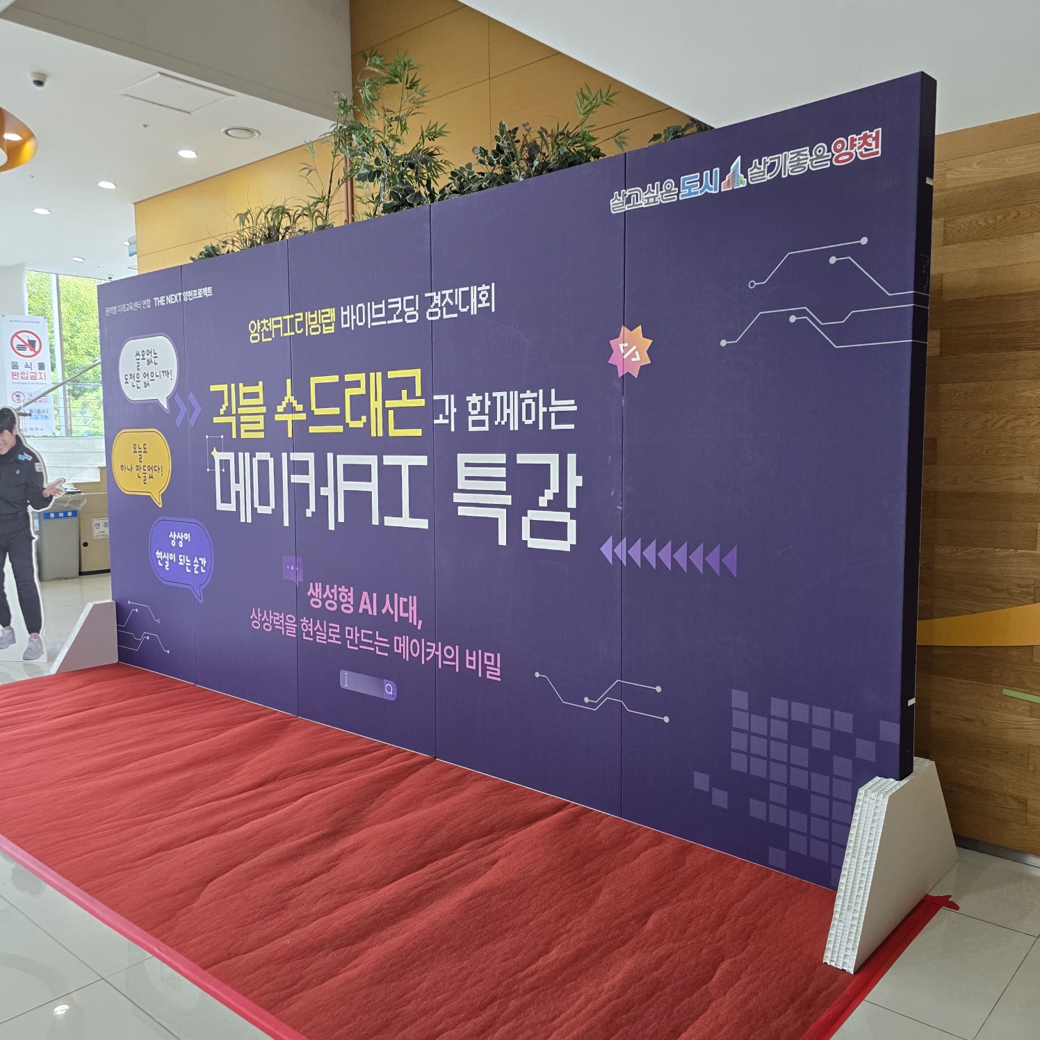 보라색 배경에 '귀블 수드레곤과 함께하는 메이커AI 특강'이 노란색·흰색으로 인쇄된 가벽. 회로 패턴 장식과 별 그래픽이 있으며, 빨간 카펫 위에 설치됨.