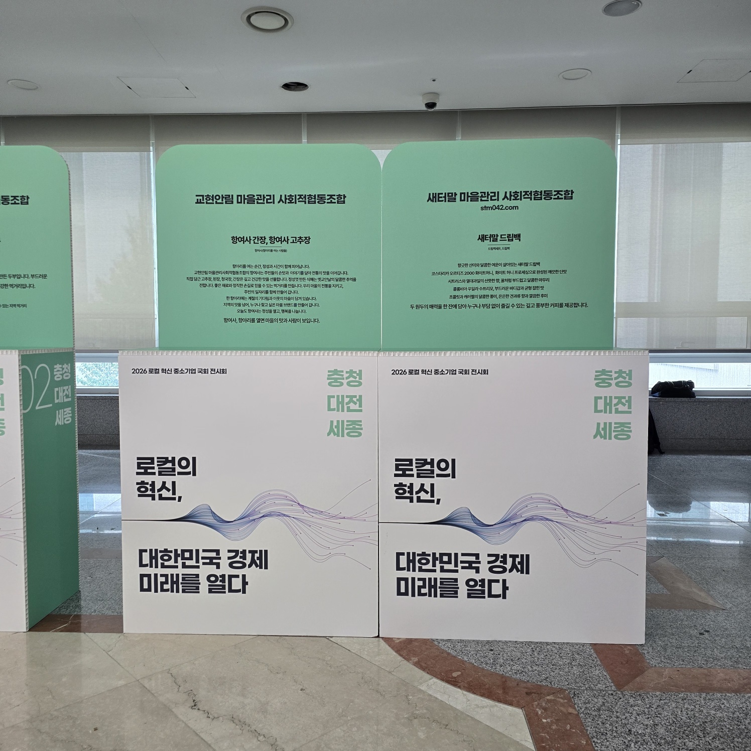 상단 라운드형 허니콤보드 가벽. 민트·베이지 색상으로 양면 인쇄. '교환안된 마을관리 사회적협동조합', '세티림 마을관리', '로컬의 혁신' 등 텍스트와 물결 그래픽 포함. 하단은 흰색 베이스.
