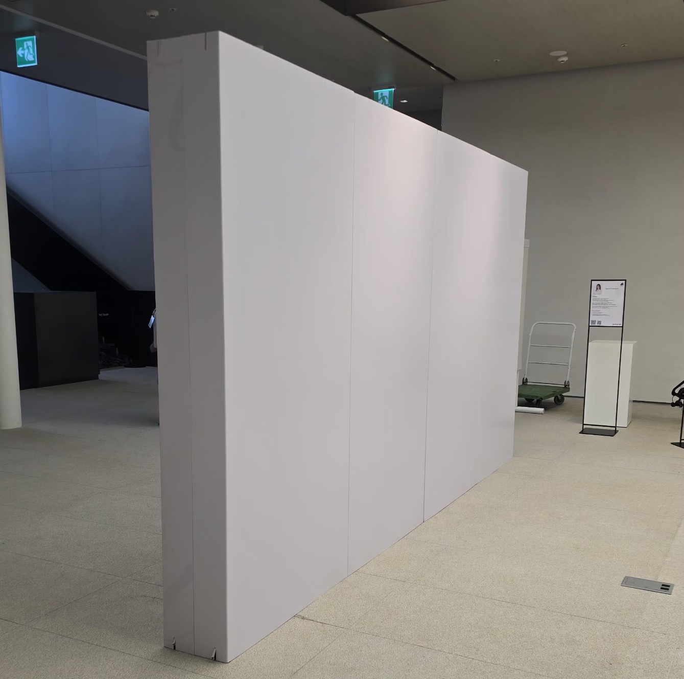 흰색 무지 대형 평면 가벽 뒷면, 인쇄 없이 백색 표면만 보임, 실내 전시장 바닥에 설치된 모습