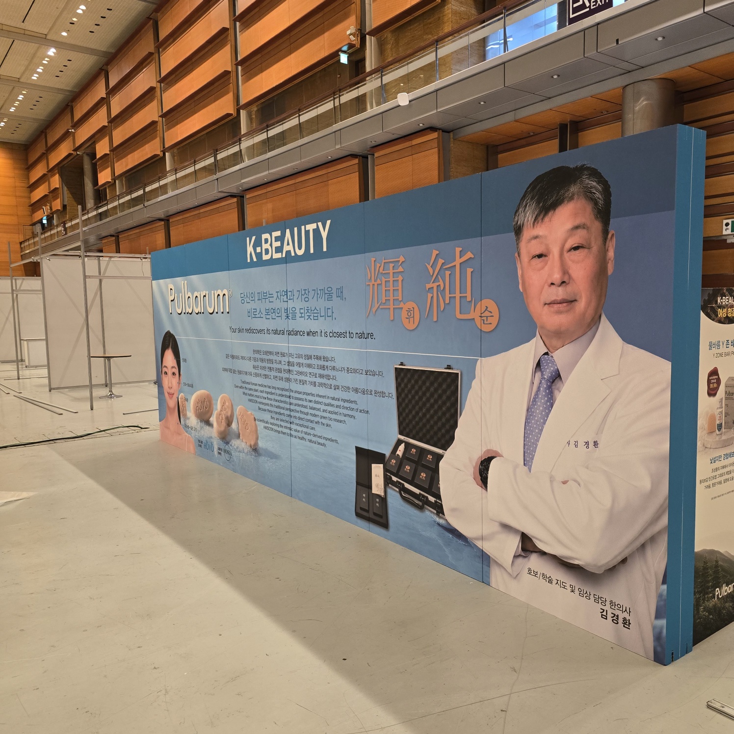 대형 허니콤 배너. 청색 상단 띠에 'K-BEAUTY', 중앙에 'Pulbarum', 한자 '輝純', 흰 가운 입은 남성 모델 사진, 제품 케이스 사진, 한글·영문 설명문 인쇄, 길이 약 5~6m 추정