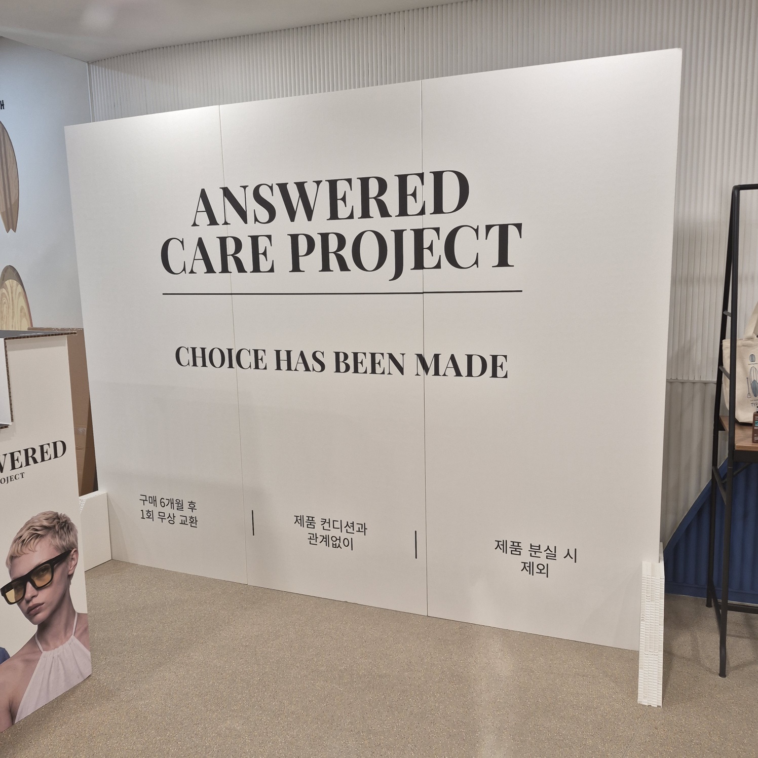 대형 백색 3연 가벽. 중앙에 'ANSWERED CARE PROJECT', 'CHOICE HAS BEEN MADE' 대형 세리프체 타이포 인쇄. 하단에 한글 설명 문구. 실내 전시 공간에 자립형으로 설치됨.