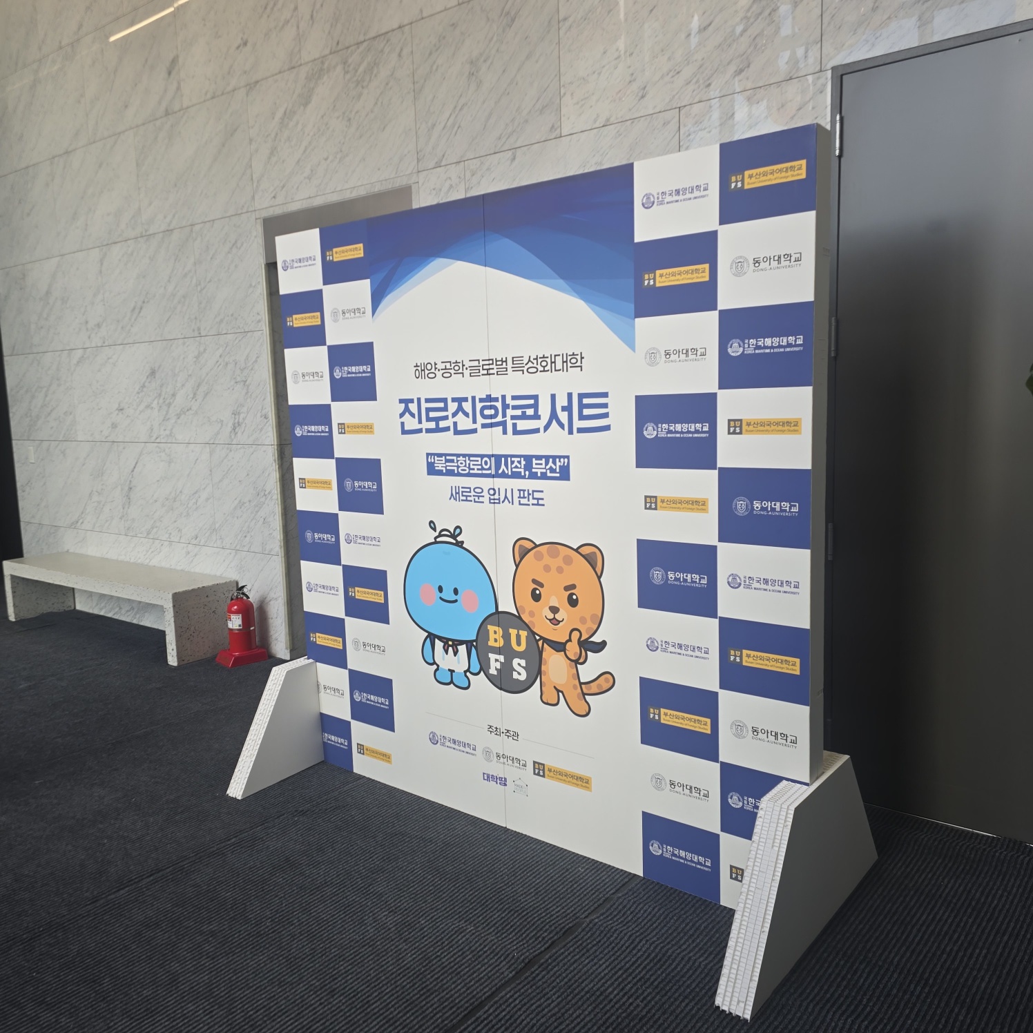 동일한 디자인의 자립형 포토존 측면 뷰. 체스판 패턴·캐릭터·타이틀 그대로이며, 뒷면 허니콤보드 구조와 흰색 하단 지지대가 드러남.